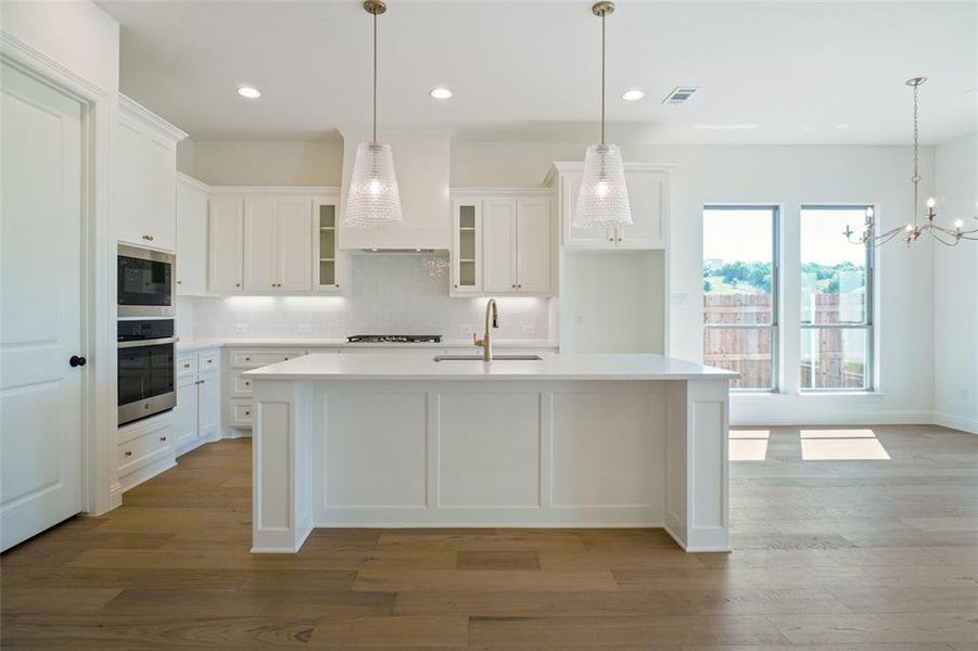 Kitchen featuring light wood finished floors, decorative backsplash, light countertops, stainless steel appliances, and white cabinetry Kitchen featuring light wood finished floors, decorative backsplash, light countertops, stainless steel appliances, and white cabinetry