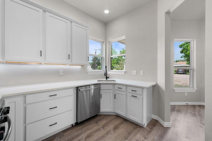 Kitchen featuring white shaker cabinetry, light-toned countertops, a stainless steel dishwasher, and a black gooseneck faucet