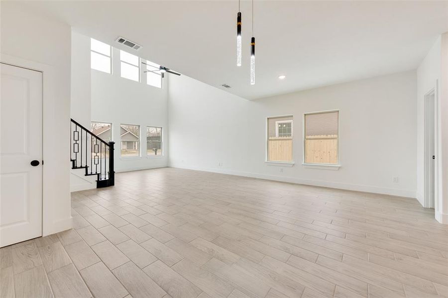 Unfurnished living room with light wood-style flooring, stairway, visible vents, and baseboards