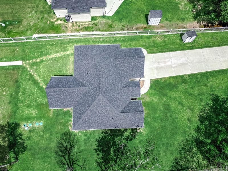 This aerial view highlights the home’s impressive curb appeal, extended driveway, fenced areas, and well-maintained outdoor space. The layout offers plenty of usable land along with additional structures that add functionality and flexibility to the property.