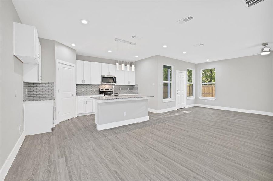 Kitchen with white cabinetry, stainless steel appliances, an island with sink, pendant lighting, and light wood-type flooring