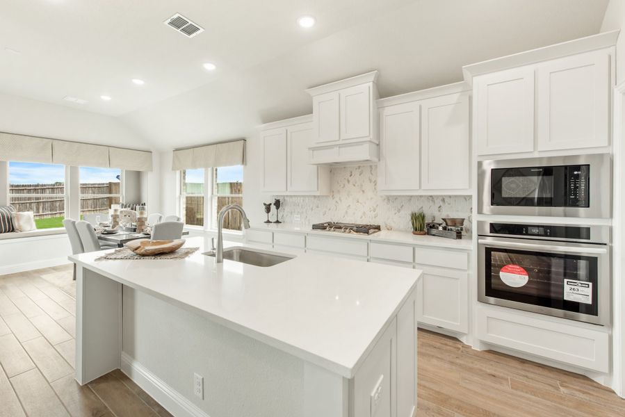 Kitchen with white cabinets, large island with sink, stainless steel appliances, and marble backsplash