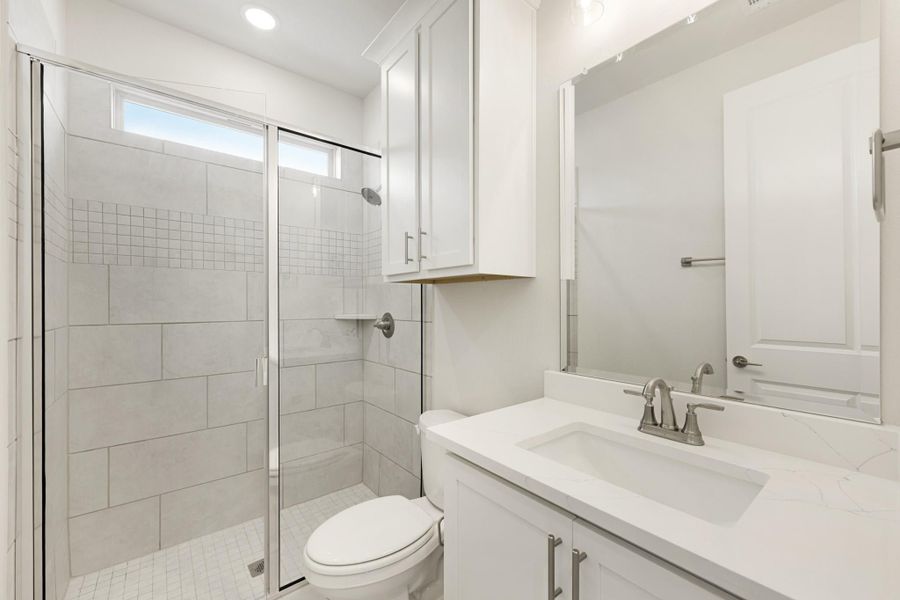 Bathroom with glass-enclosed tile shower, white vanity with quartz countertop, and toilet