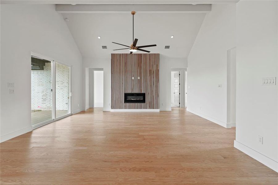 Unfurnished living room with high vaulted ceiling, a ceiling fan, beam ceiling, light wood-type flooring, and a glass covered fireplace Unfurnished living room with high vaulted ceiling, a ceiling fan, beam ceiling, light wood-type flooring, and a glass covered fireplace