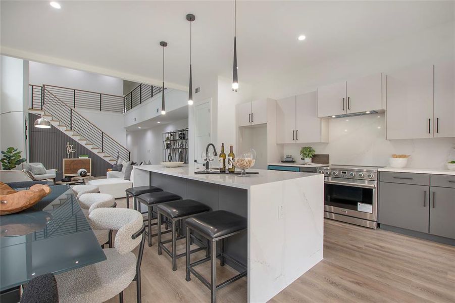 Kitchen featuring light wood-type flooring, electric range, hanging light fixtures, a center island with sink, and gray cabinetry