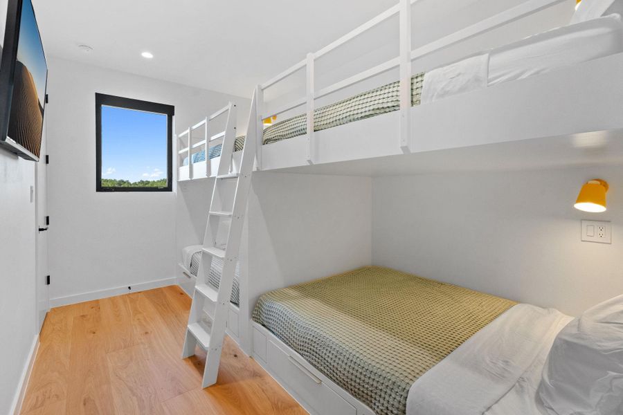 Bright room with bunk beds, light wood-finish flooring, and a single window with black trim