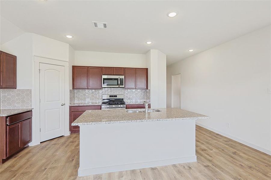 Kitchen featuring sink, tasteful backsplash, light hardwood / wood-style flooring, an island with sink, and appliances with stainless steel finishes