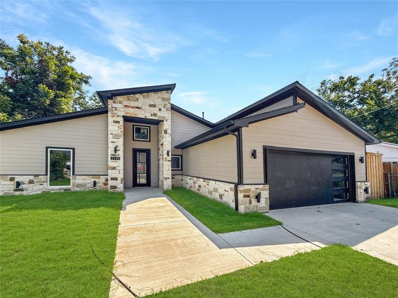 View of front of house featuring stone siding, driveway, a front lawn, and a garage