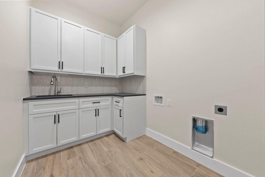 Functional laundry space featuring crisp cabinetry, a sink, and connections for appliances.