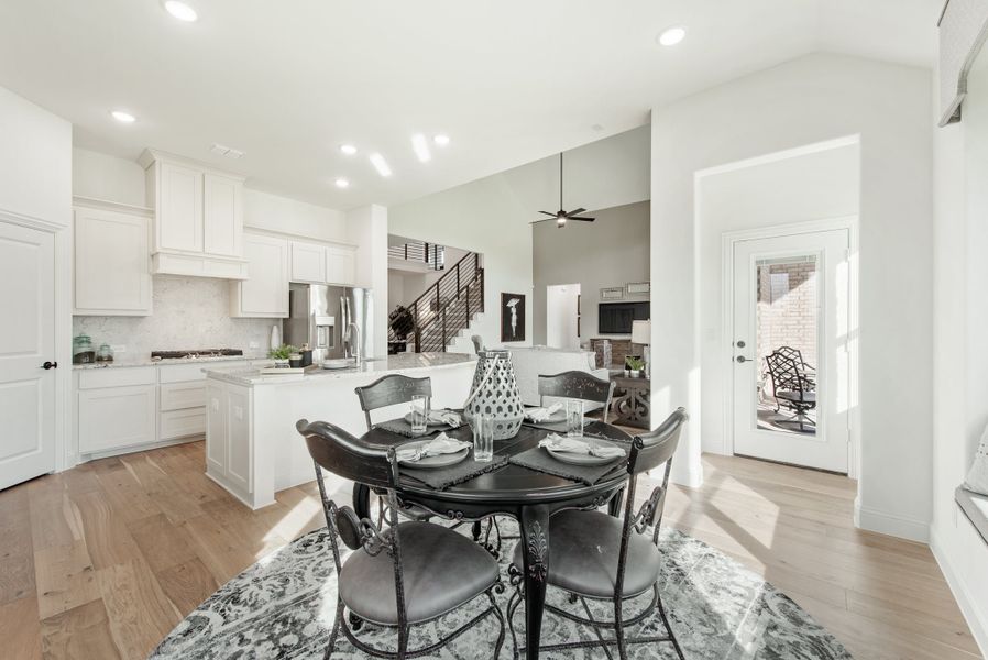 Open-concept dining area with round black table, hardwood floors, and white kitchen in background Open-concept dining area with round black table, hardwood floors, and white kitchen in background