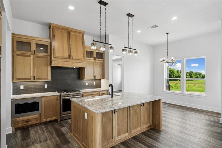 Kitchen with stainless steel appliances, dark wood-type flooring, decorative backsplash, a center island with sink, and a chandelier
