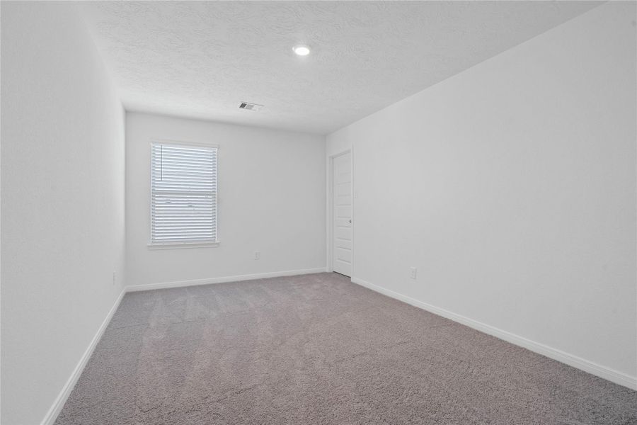 This secondary bedroom offers comfort and style with plush carpeting, neutral paint tones, recessed lighting, a large window with blinds, and a walk-in closet.