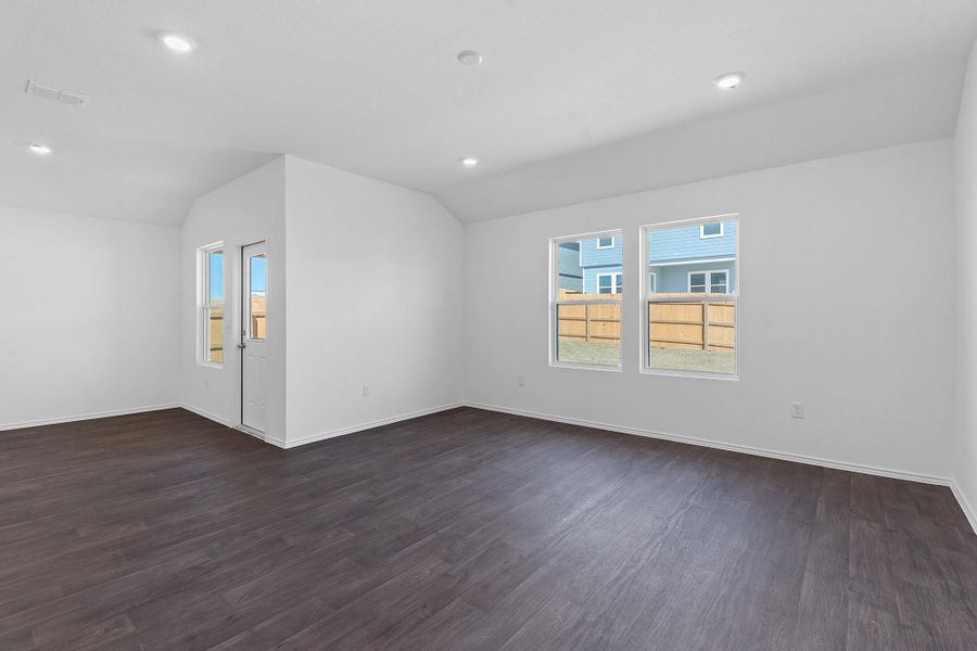 Unfurnished room featuring a healthy amount of sunlight, dark wood-style floors, visible vents, and vaulted ceiling