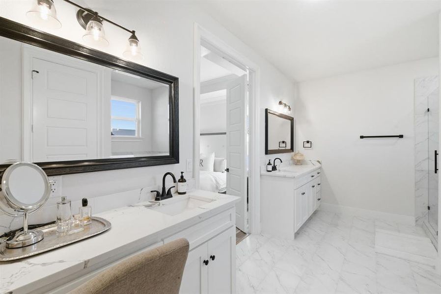Ensuite bathroom featuring two vanities, light marble finish floors, and a marble finish shower