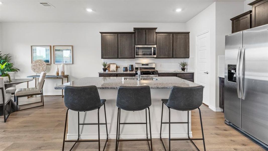 Open-concept kitchen featuring a spacious island with granite countertop, dark wood-finish cabinetry, stainless steel appliances, and wood-finish flooring Open-concept kitchen featuring a spacious island with granite countertop, dark wood-finish cabinetry, stainless steel appliances, and wood-finish flooring