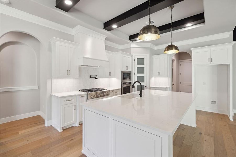 Kitchen featuring decorative light fixtures, white cabinetry, and premium range hood