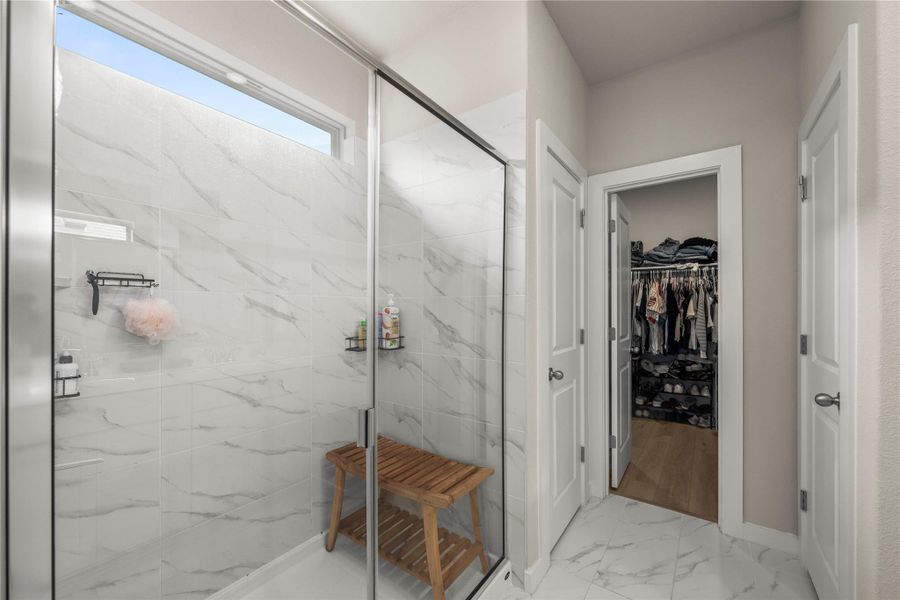 Marble-tiled shower with clear glass enclosure and an adjacent walk-in closet. Marble-tiled shower with clear glass enclosure and an adjacent walk-in closet.