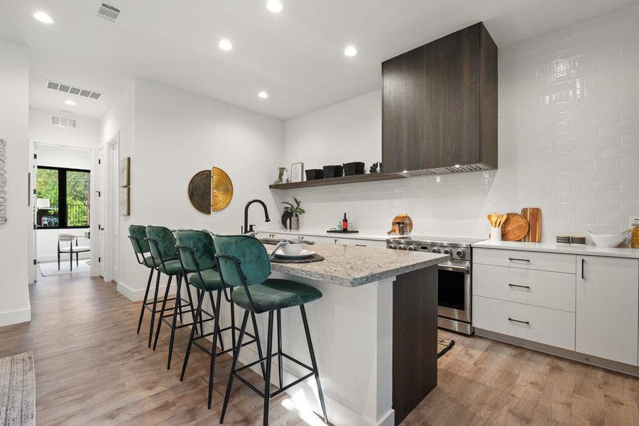 Kitchen with dark brown cabinets, a breakfast bar, modern cabinets, electric stove, and light stone countertops