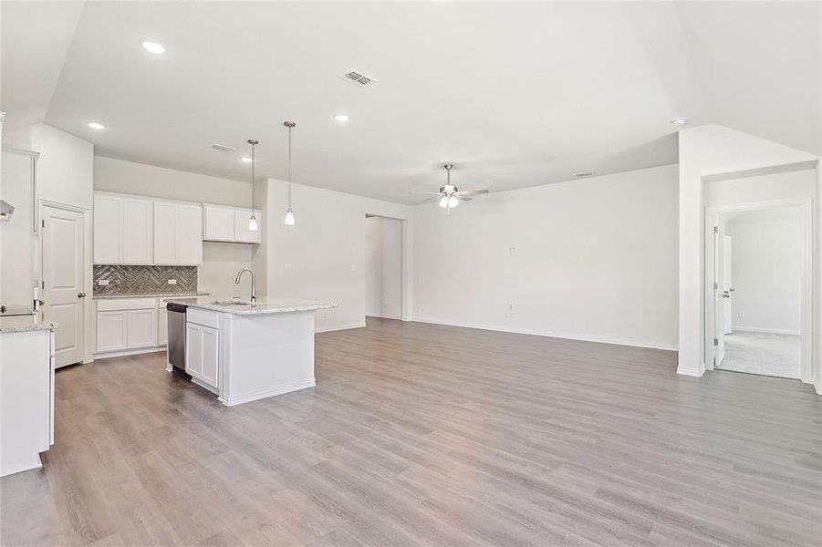 Kitchen featuring light hardwood / wood-style flooring, a center island with sink, dishwasher, decorative backsplash, and white cabinetry