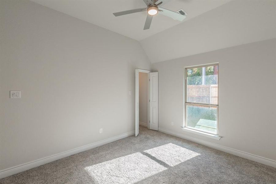 Unfurnished bedroom featuring ceiling fan, lofted ceiling, and light carpet