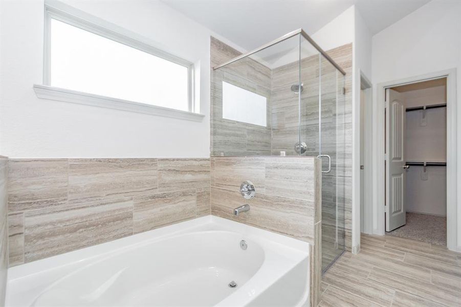 Step into elegance with this luxurious primary bathroom featuring a spa-like soaking tub and a frameless glass-enclosed walk-in shower. The tile surround creates a polished, modern look, while the frosted window provides natural light and privacy. This bathroom is your personal retreat for relaxation and rejuvenation.