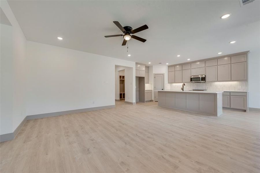 Unfurnished living room with sink, ceiling fan, and light hardwood / wood-style floors