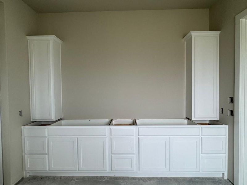Expansive white shaker-style vanity cabinetry featuring multiple drawers and under-sink storage, complemented by two tall storage cabinets