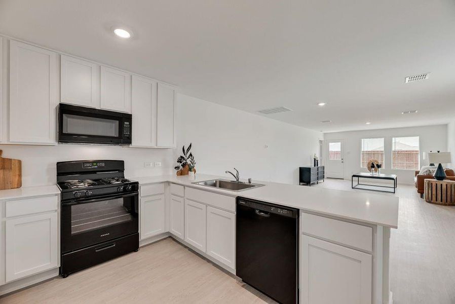 Kitchen with black appliances, open floor plan, light countertops, white cabinets, and recessed lighting