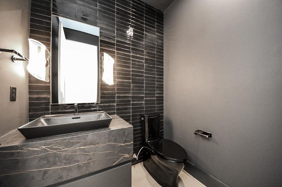 Stylish half bath with a striking black tiled accent wall, unique vessel sink, and upscale lighting for a bold, sophisticated look.