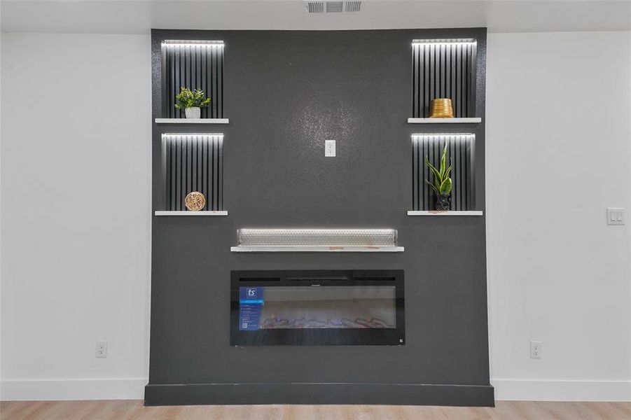 Integrated electric fireplace with a dark accent wall, recessed lighting, built-in shelving, and light wood-finish flooring Integrated electric fireplace with a dark accent wall, recessed lighting, built-in shelving, and light wood-finish flooring