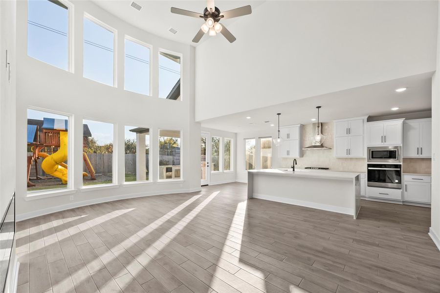 This spacious, light-filled open-plan living area features high ceilings and large windows that overlook a backyard with a play structure. The modern kitchen includes sleek white cabinetry, stainless steel appliances, and a central island, perfect for family gatherings and entertaining. This spacious, light-filled open-plan living area features high ceilings and large windows that overlook a backyard with a play structure. The modern kitchen includes sleek white cabinetry, stainless steel appliances, and a central island, perfect for family gatherings and entertaining.