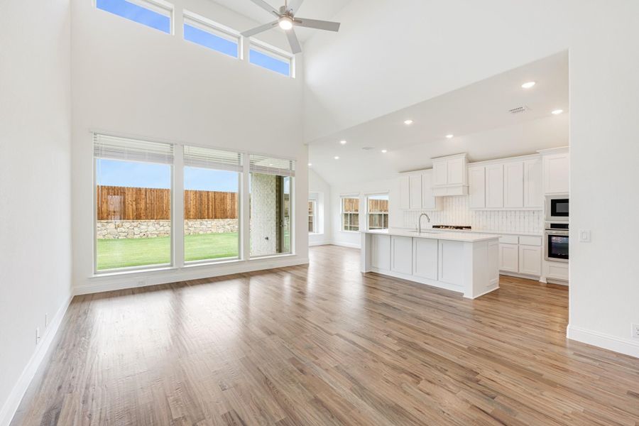 Open living area with high ceilings and hardwood floors flowing into white kitchen with island Open living area with high ceilings and hardwood floors flowing into white kitchen with island
