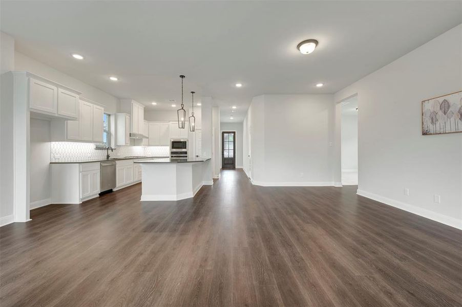 Kitchen with open floor plan, white cabinetry, dark wood-type flooring, and stainless steel dishwasher