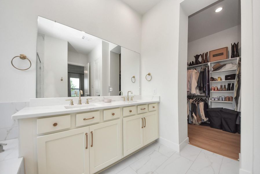 Elegant bathroom with a double vanity, sleek fixtures, and a spacious walk-in closet offering ample storage.