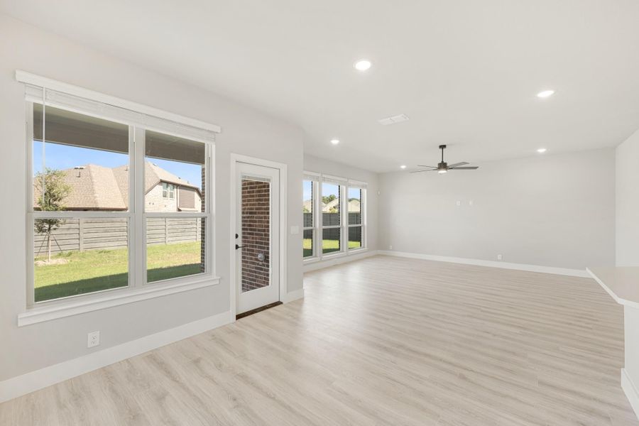 Open living room with light wood floors, ceiling fan, and large windows overlooking backyard