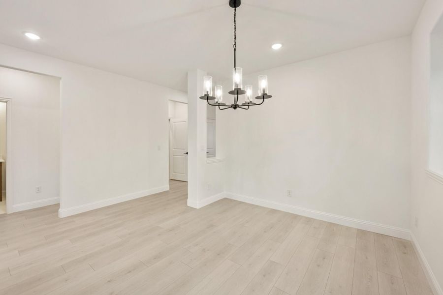 Empty dining room with light wood floors, white walls, and a black chandelier overhead Empty dining room with light wood floors, white walls, and a black chandelier overhead