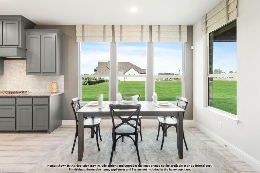 Breakfast nook with wood dining table, four chairs, and large windows overlooking a green backyard next to gray kitchen cabinets.