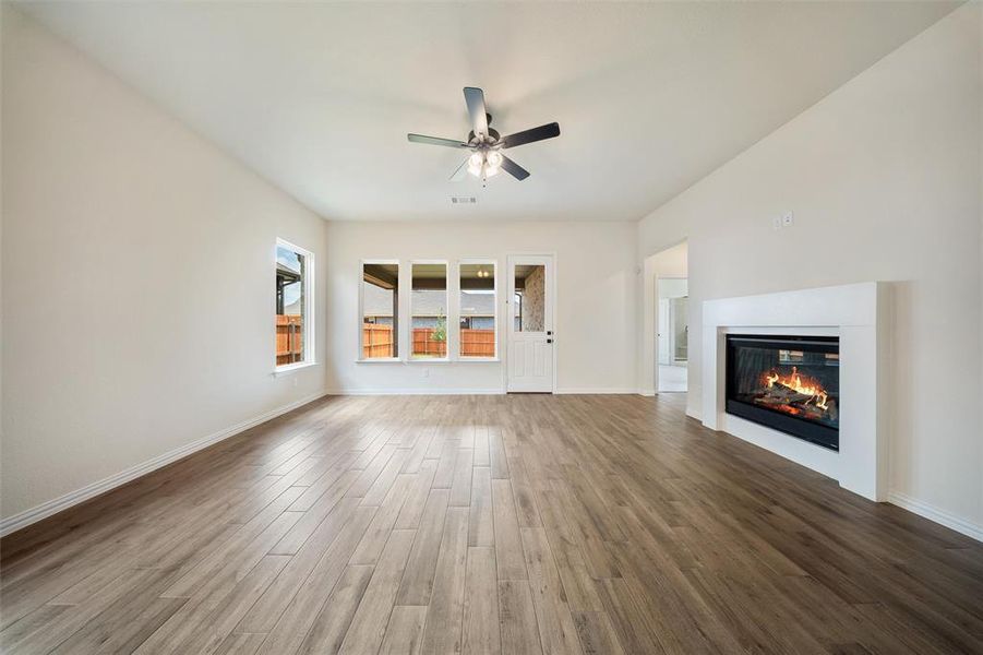 Unfurnished living room featuring a ceiling fan, wood finished floors, and a glass covered fireplace