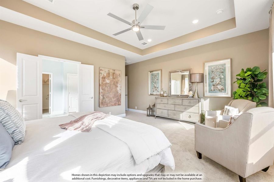 Spacious master bedroom with tray ceiling, ceiling fan, carpet flooring, and walk-in closet entrance