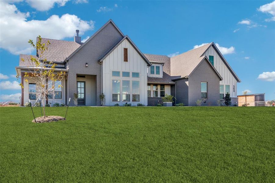 Rear view of house with board and batten siding, a lawn, roof with shingles, and brick siding Rear view of house with board and batten siding, a lawn, roof with shingles, and brick siding