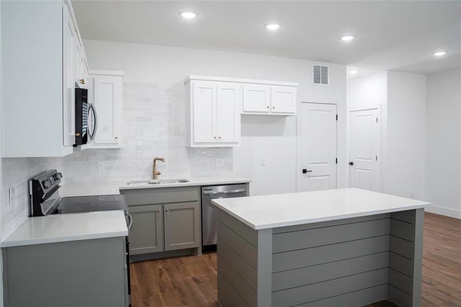 Kitchen with dark hardwood / wood-style flooring, gray cabinetry, stainless steel appliances, sink, and a kitchen island