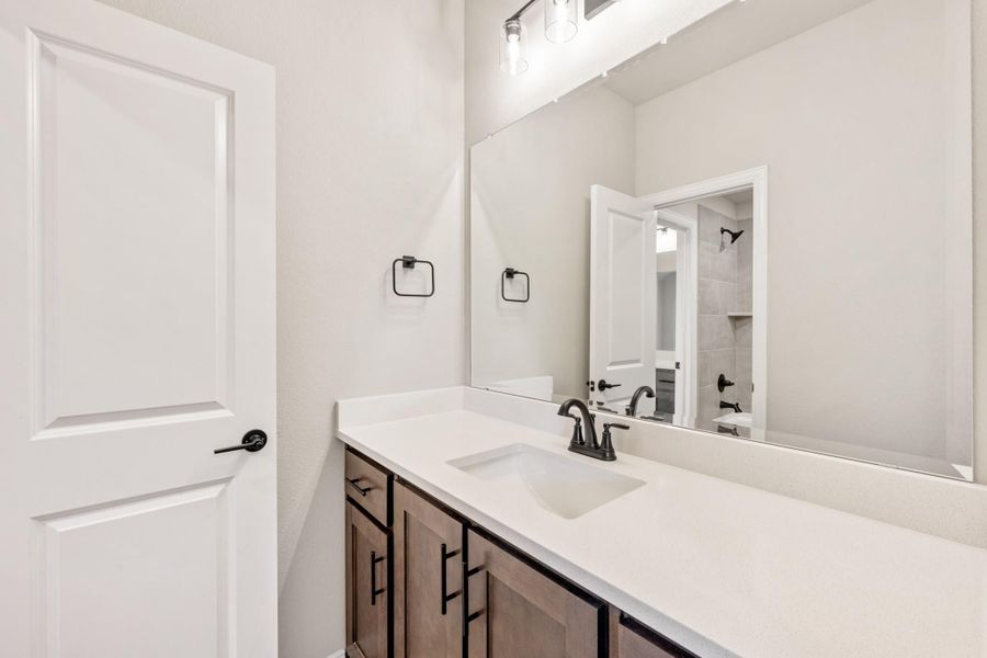 Bathroom vanity with white quartz countertop, wood cabinets, black fixtures, and large mirror above sink
