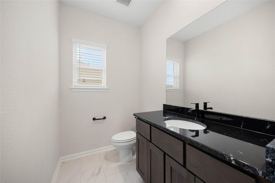 Convenient second-story half bath perfectly positioned between the game room and media room hubs. This highly functional space features a deep espresso-toned vanity topped with high-contrast black granite countertops, an undermount sink, and a modern matte black faucet. Complete with a large vanity mirror, sleek matte black hardware, a privacy window with blinds, and upscale marble-look floor tile, this powder room offers maximum comfort for upstairs entertaining. Convenient second-story half bath perfectly positioned between the game room and media room hubs. This highly functional space features a deep espresso-toned vanity topped with high-contrast black granite countertops, an undermount sink, and a modern matte black faucet. Complete with a large vanity mirror, sleek matte black hardware, a privacy window with blinds, and upscale marble-look floor tile, this powder room offers maximum comfort for upstairs entertaining.