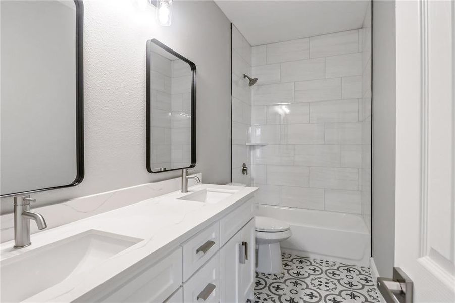 Full bathroom featuring tile patterned floors, tiled shower / bath, toilet, and dual bowl vanity