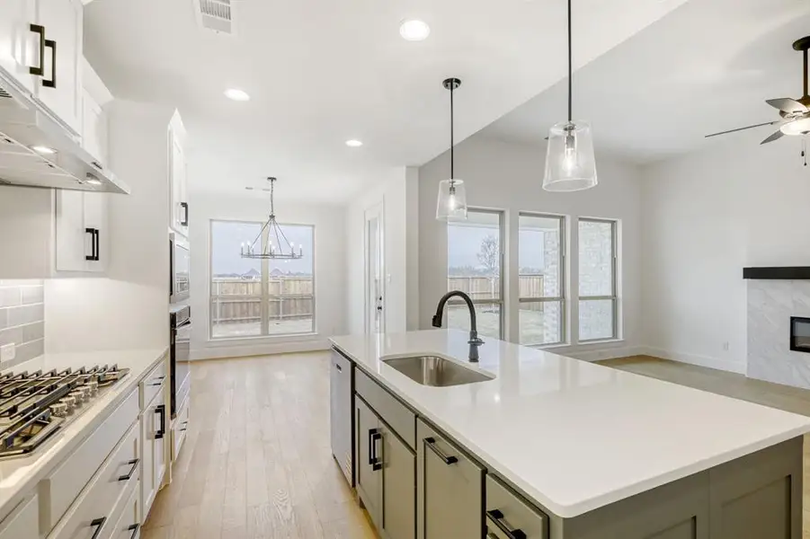 Kitchen featuring an island with sink, light wood-style floors, a premium fireplace, stainless steel appliances, and a ceiling fan