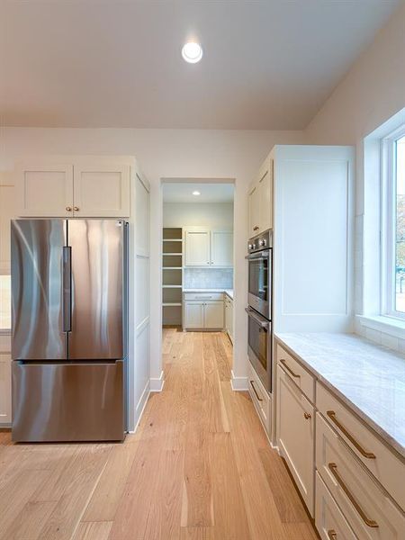 Kitchen featuring light wood-finish flooring, white cabinetry with brushed gold hardware, stainless steel appliances, and light-toned countertops