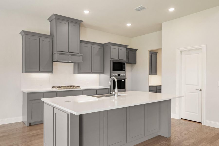 Kitchen with gray shaker cabinets, white countertops, large island with sink, and stainless steel appliances on wood floors Kitchen with gray shaker cabinets, white countertops, large island with sink, and stainless steel appliances on wood floors