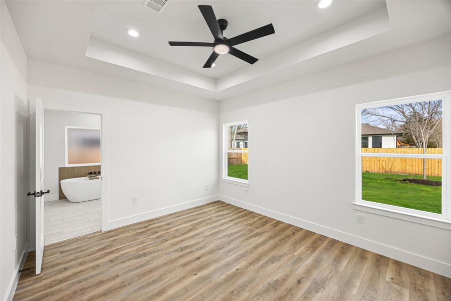 Spacious retreat with tray ceiling, ceiling fan, and large windows overlooking the backyard.