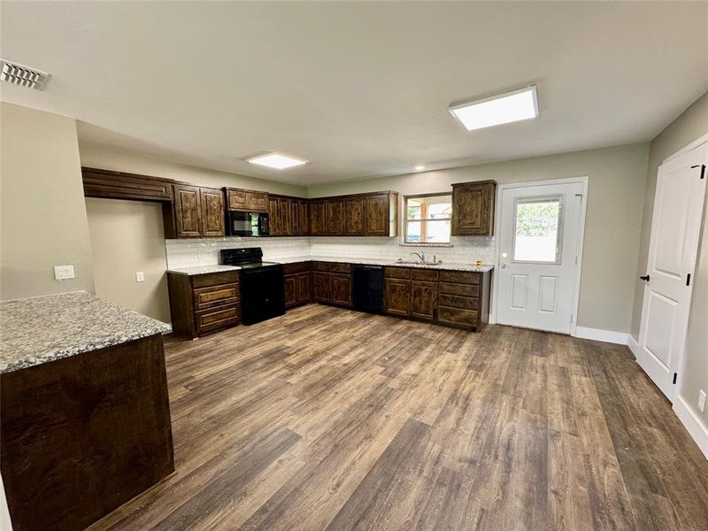 Kitchen featuring decorative backsplash, dark brown cabinets, black appliances, and dark wood-style floors