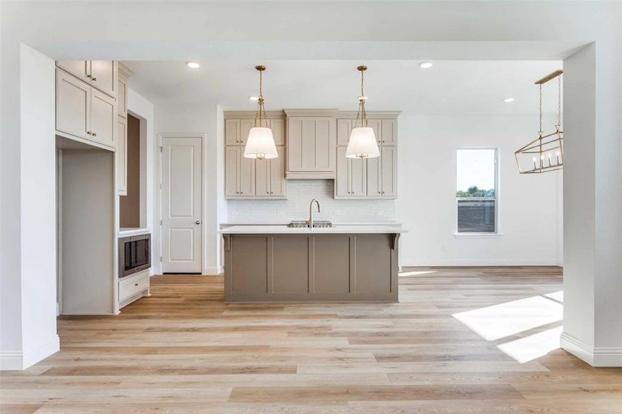 Kitchen featuring decorative light fixtures, backsplash, a center island with sink, recessed lighting, and light wood-style flooring